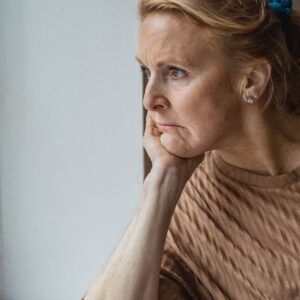 Thoughtful mature woman by a window β signs of low estrogen after hysterectomy