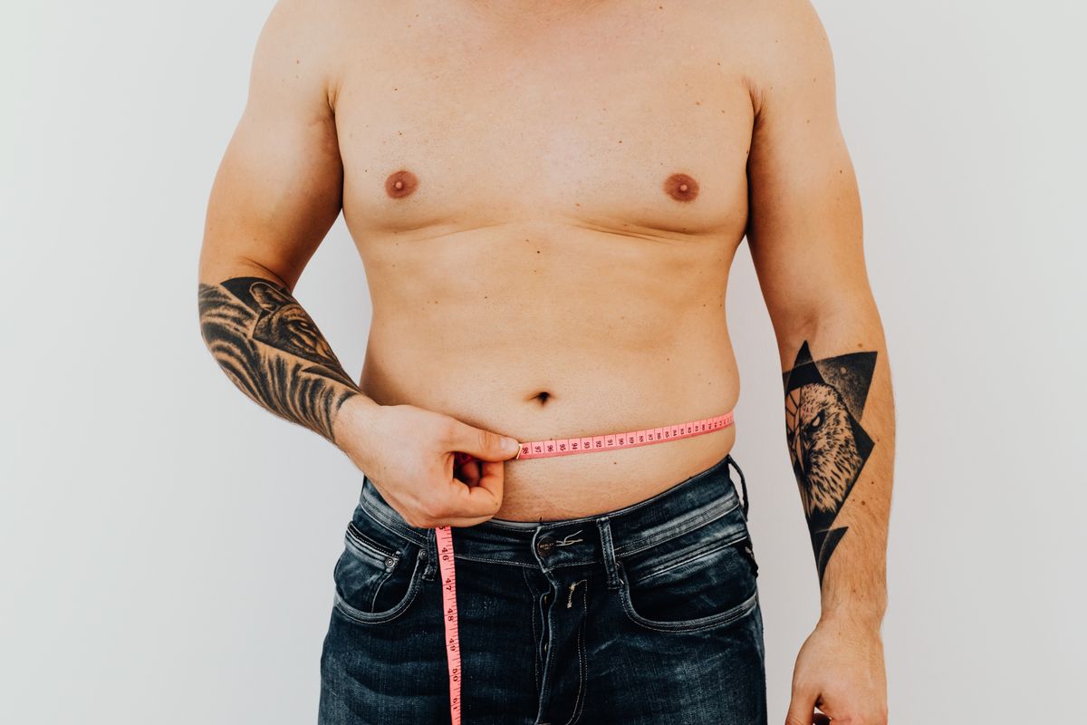 Man measuring his waistline with a tape measure — low testosterone and weight gain