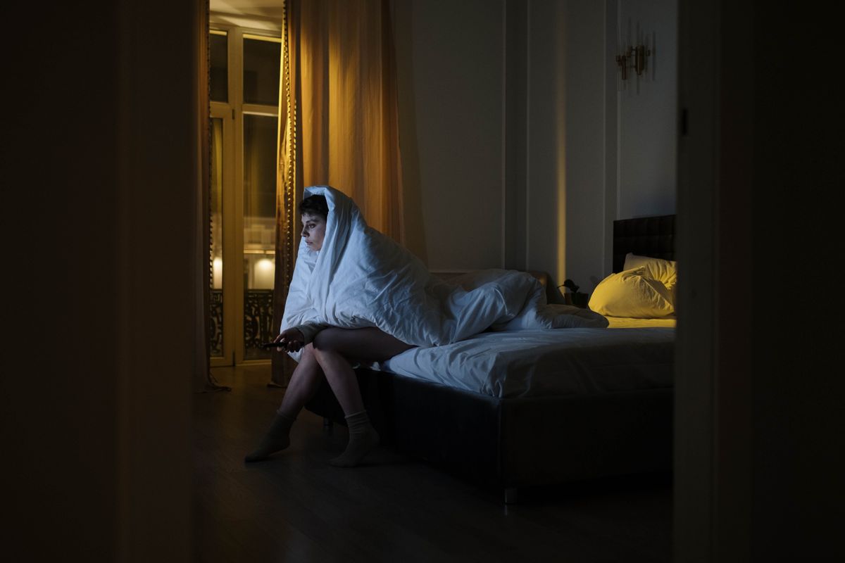 Woman sitting awake in bed at night wrapped in a blanket — night sweats